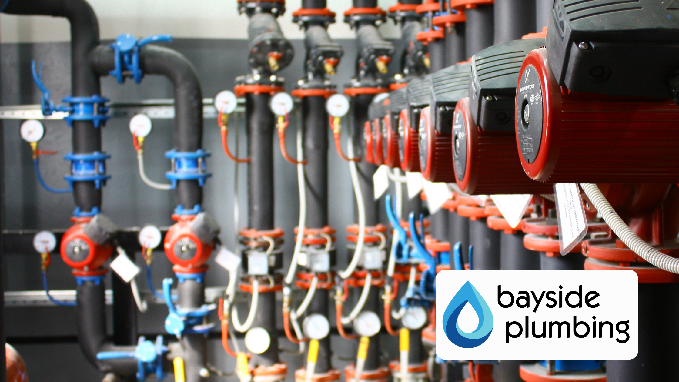 Large-scale commercial plumbing piping manifold and water pressure pumps with the Bayside Plumbing logo overlay.