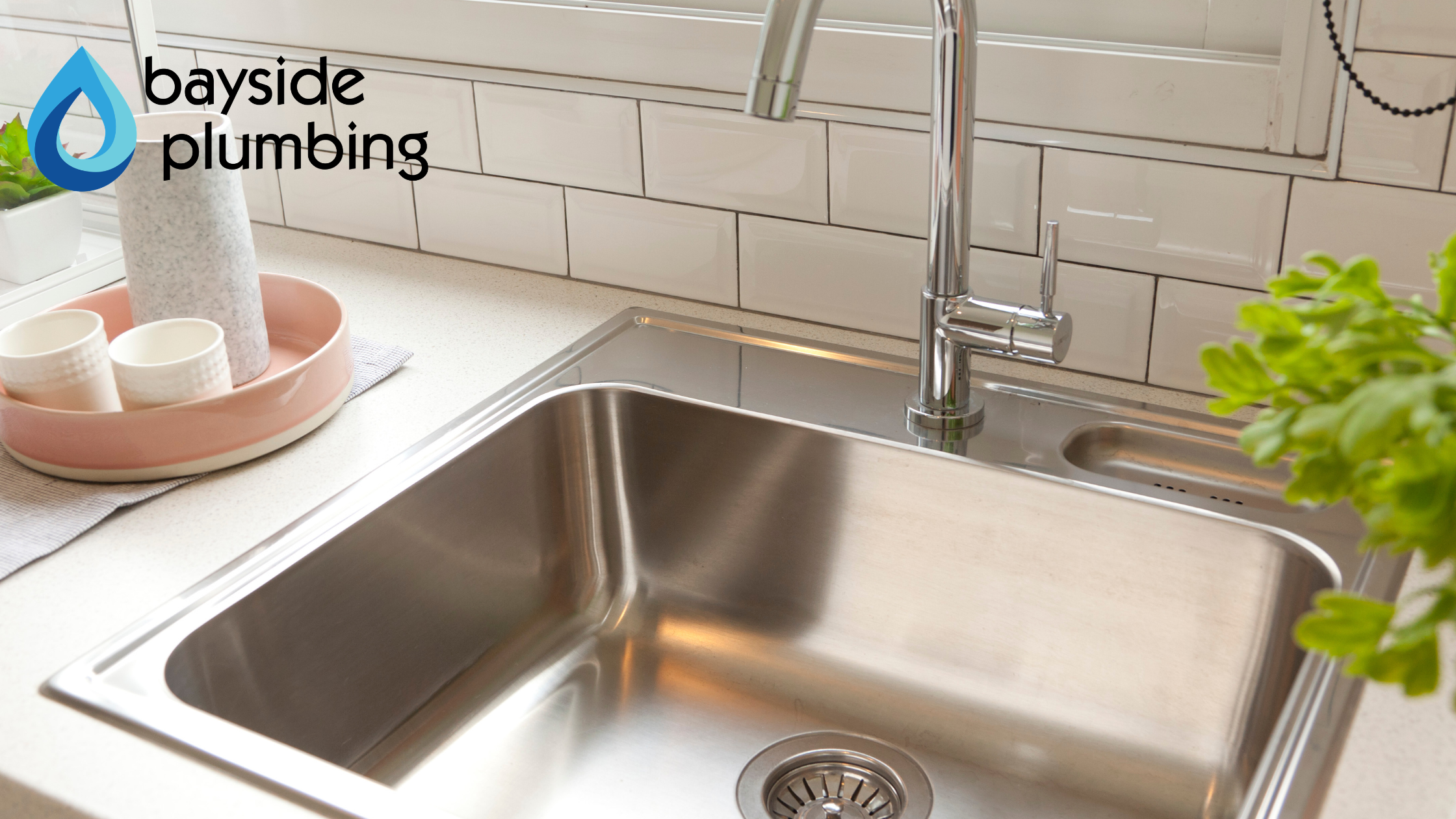 A spotless stainless steel kitchen sink and chrome faucet with the Bayside Plumbing logo overlay.